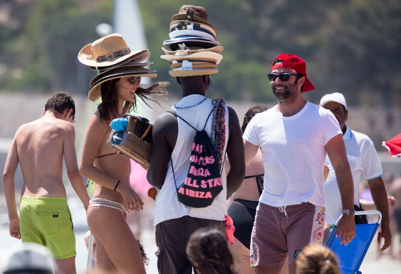 Alessandra Ambrosio lleva más de una semana en las playas de Ibiza disfrutando del verano español. Aquí, la modelo de 36 años bromea con un vendedor de sombreros en la playa.