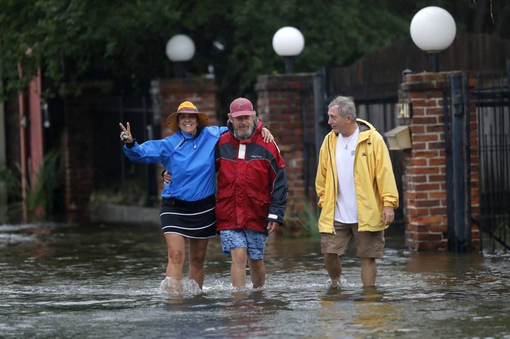 Isabelle Schneidau, izquierda, hace un gesto a la cámara mientras camina en una marea de tormenta ascendente con Mont Echols, centro, y L.G. Sullivan, derecha, después de revisar sus barcos en la sección West End de Nueva Orleans antes de la tormenta tropical Cristóbal.