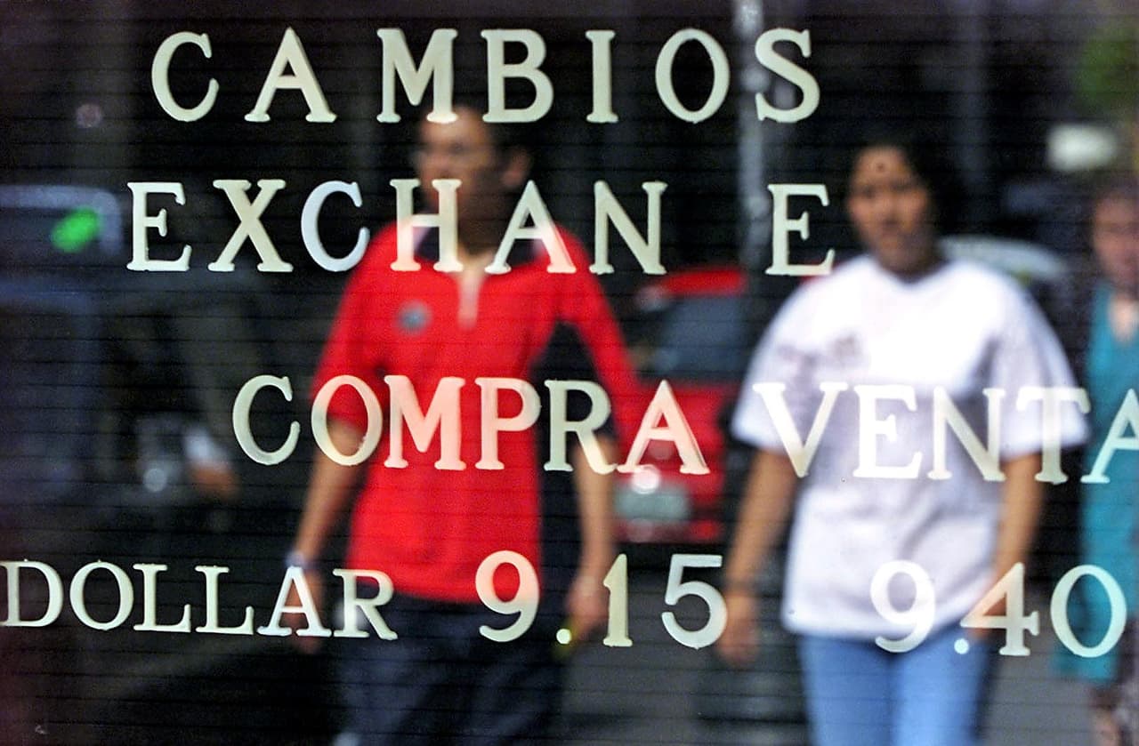 Una pareja pasa caminando frente a una pizarra de una casa de cambio de moneda con la cotizacion del dolar, en Ciudad de Mexico el 12 de julio de 2001. Para ese momento, el peso mexicano estaba presionado por la crisis económica en Argentina, que ese año terminó en la imposición de un "corralito" (la restricción de los retiros de dinero en efectivo) y la renuncia del presidente Fernando de la Rúa. (Ramón Cavallo / AFP)
<br>