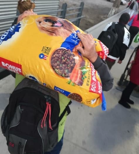 Un hombre cruza a pie la frontera con un costal de alimentos para perros.