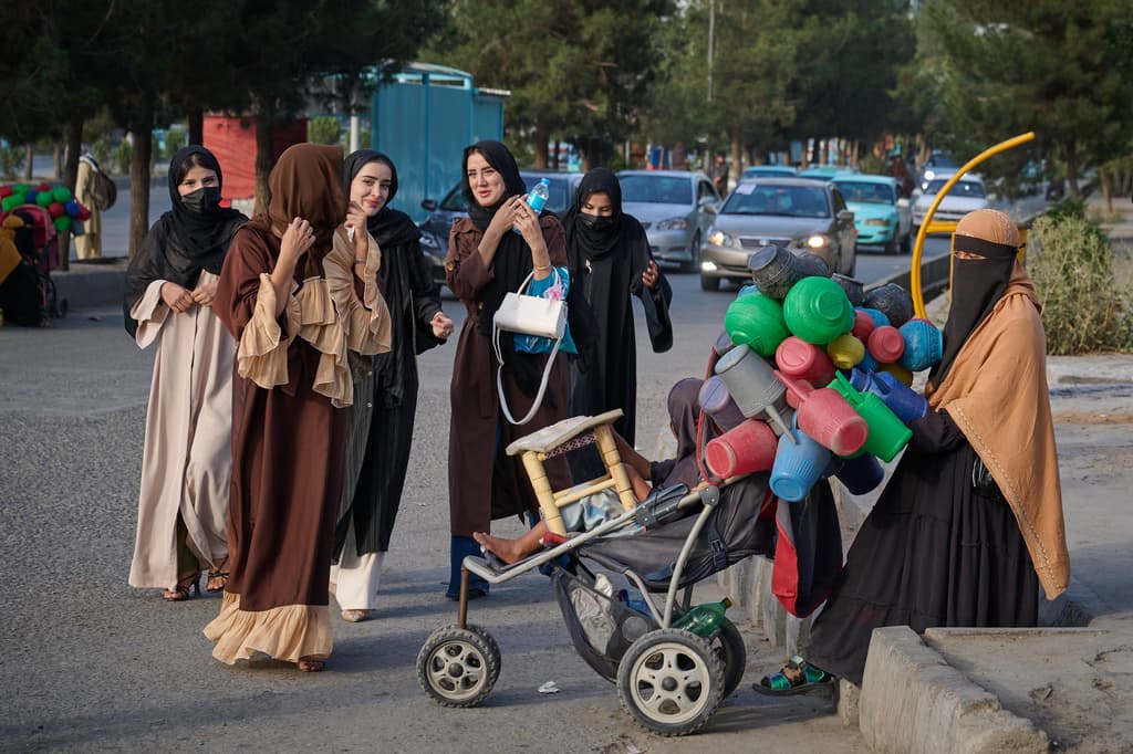Un grupo de mujeres jóvenes pasa junto a una mujer que vende garrafas de agua de plástico en una calle, en vísperas del quinto aniversario de la retirada de Estados Unidos.