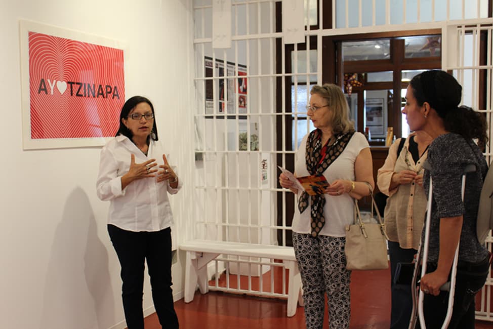 Marietta Bernstorff, de SPARC, con un grupo de visitantes a la exhibición en honor a los normalistas de Ayotzinapa.