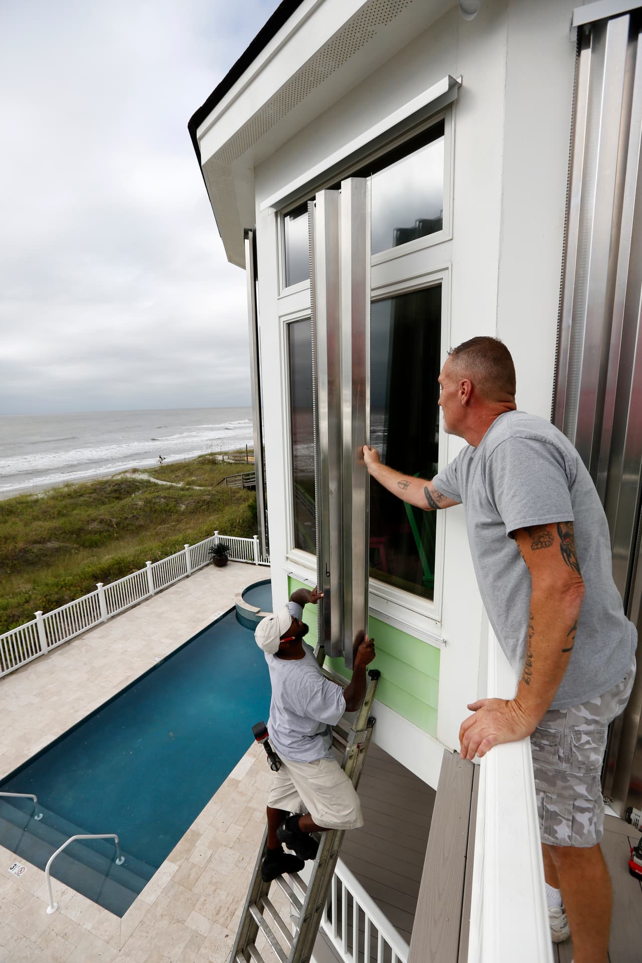 Dimitri Pinckney y Bob Corbin instalan paneles de protección contra huracanes en las ventanas de una casa en Isle of Palms, Carolina del Sur.