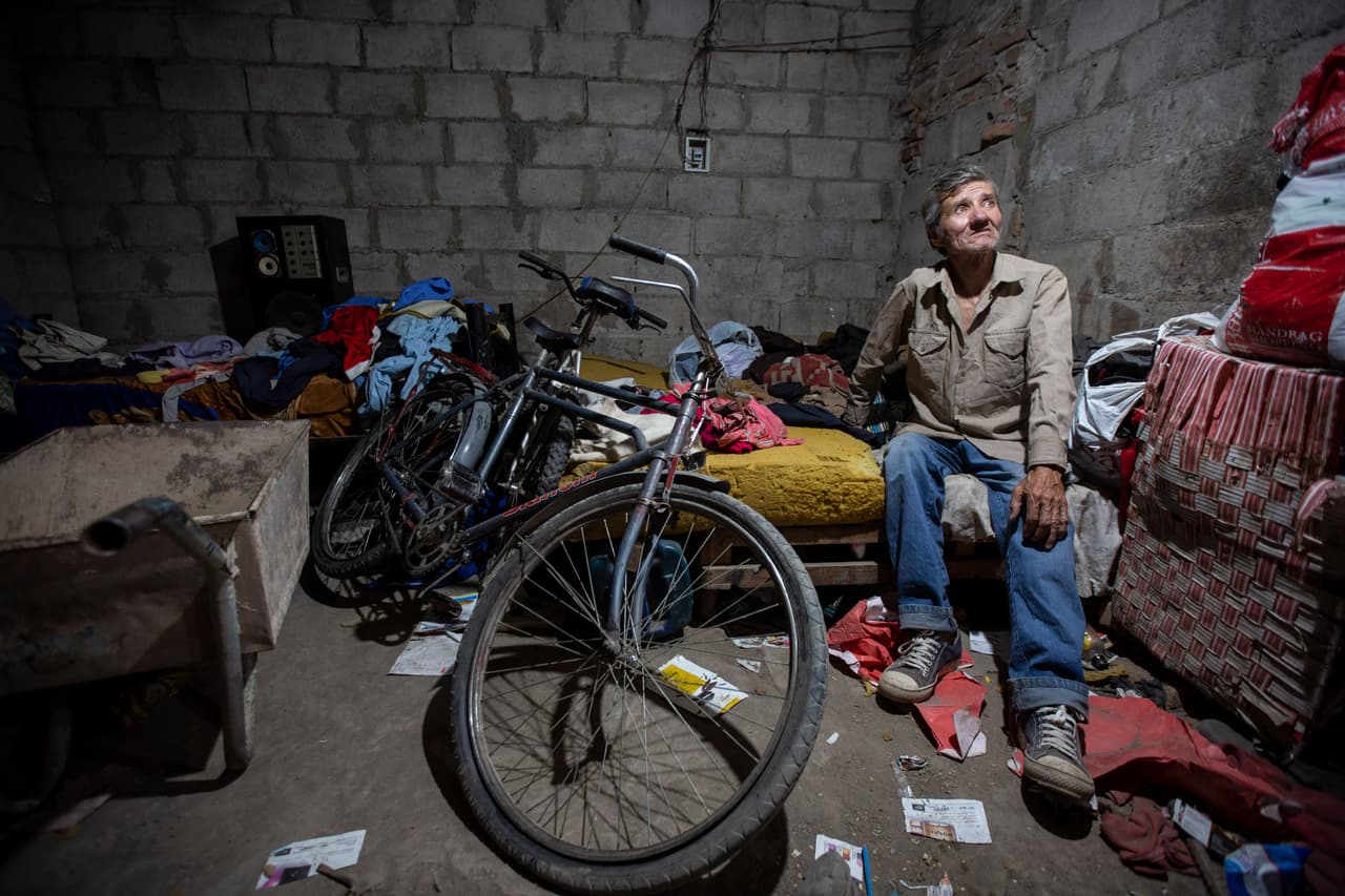 <b>Carlos Araya</b> vive en una casucha de bloques de hormigón en San Justo, un barrio pobre de la provincia de Salta. Su familia de ocho miembros comparte una cama y cocina con leña. Hace cuatro años, este hombre de 62 años mantenía a su familia trabajando como pintor y jardinero, y pagaba por un terreno donde empezó a construir una casita. Pero en el 2017 la economía se vino abajo, perdió lo que había invertido y se esfumó su sueño de salir de la pobreza. Construyó él mismo la casucha donde vive ahora. Sus hijos reciben una comida en la escuela. En la casa, se come solo arroz y papas. Apenas sobreviven con lo que gana la esposa de Araya vendiendo cosméticos y con una pensión por incapacidad.