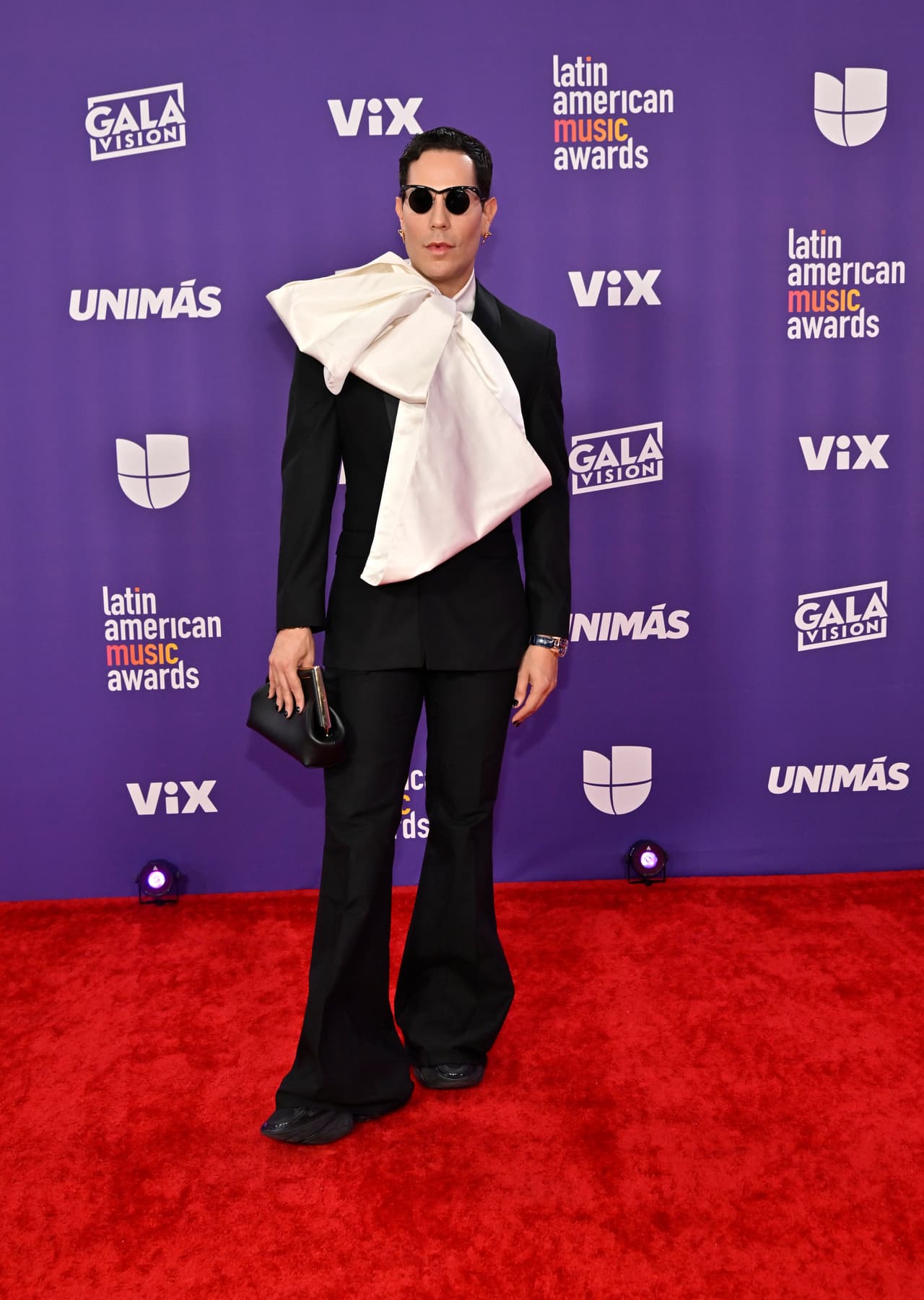 <b>Christian Chávez </b>
<br>
<br>Sumándose a la tendencia de los looks extravagantes, el cantante lució un traje negro con un moño blanco de gran tamaño que cubría todo el saco.