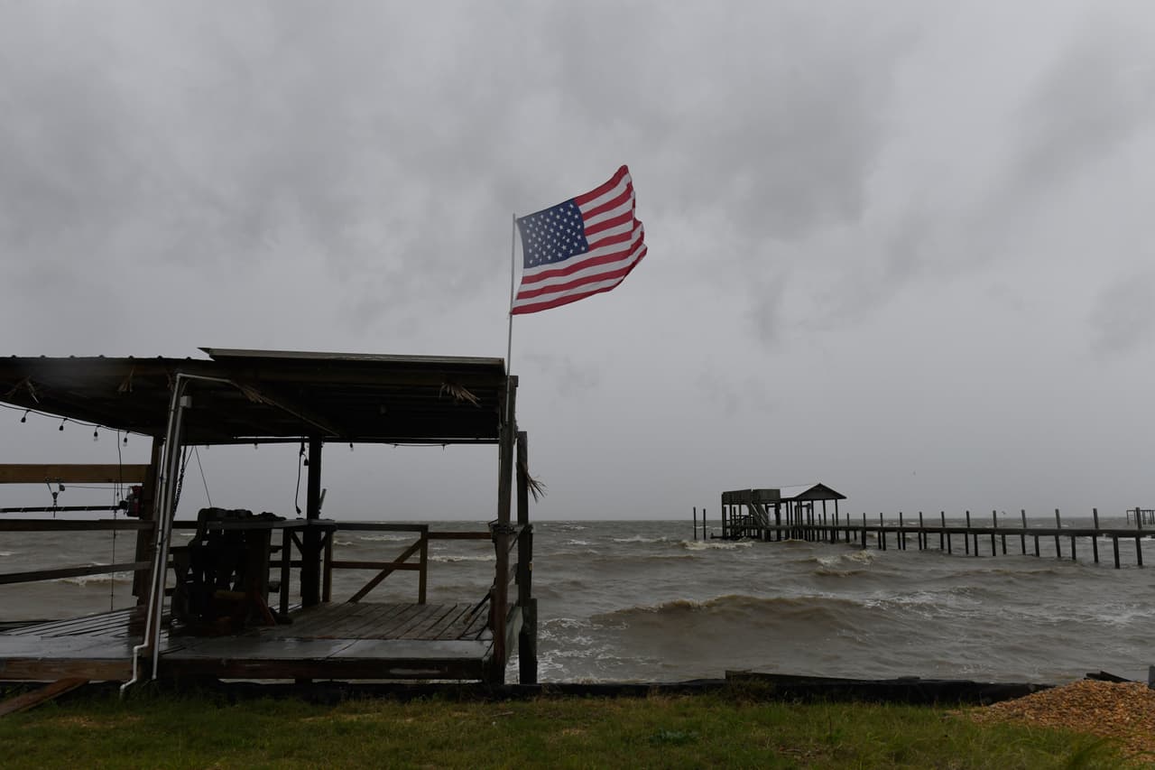 Una bandera estadounidense ondea al viento generado por los efectos del huracán Isaias en una playa desierta el viernes 9 de octubre de 2026, en la isla Mon Louis, Alabama.