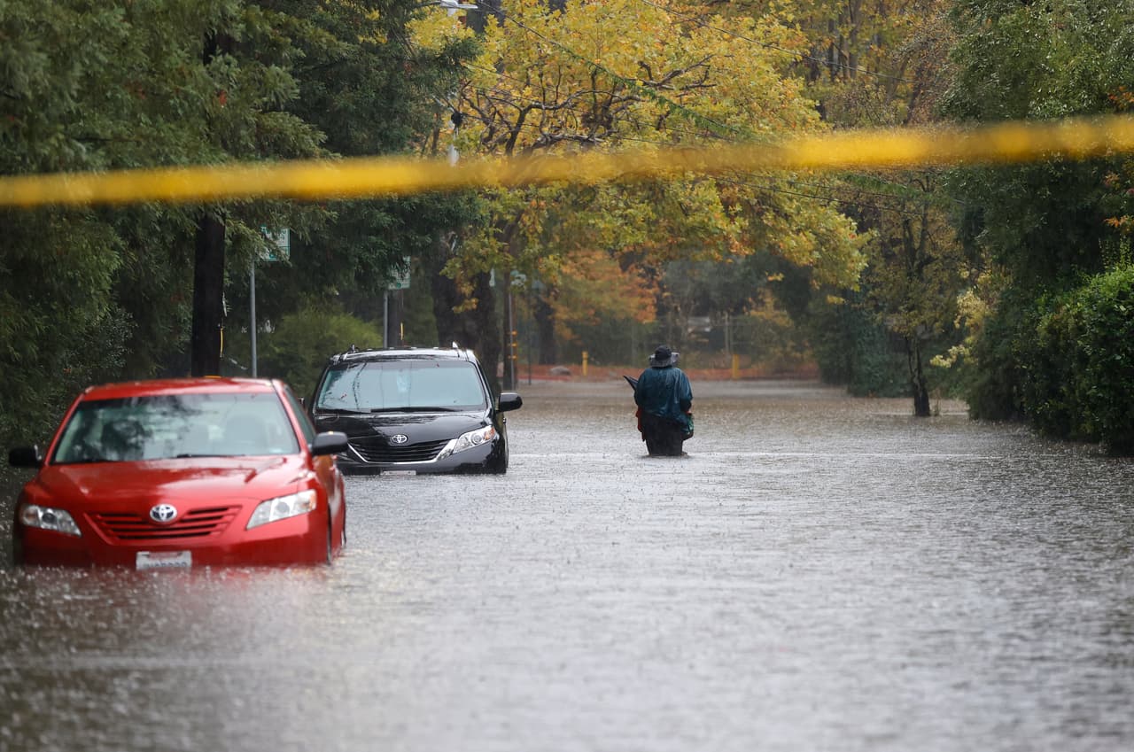 <b>Kentfield. </b>Un peatón camina en una calle inundada mientras el agua llega hasta la defensa de un par de autos estacionados.