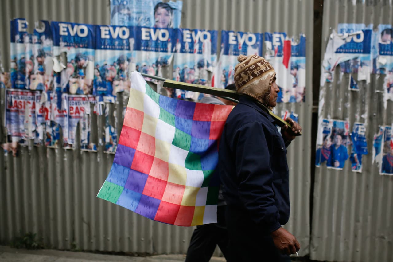 Un seguidor de Evo Morales camina con una whipala al hombro.