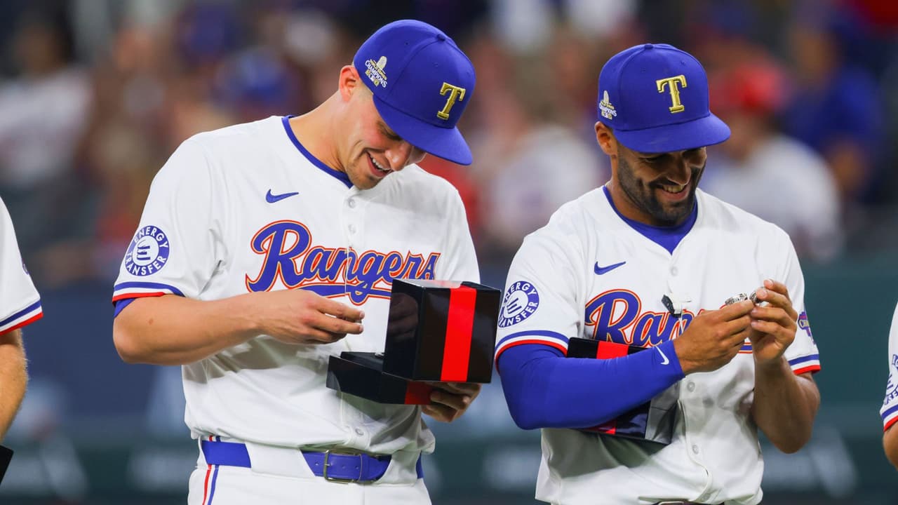 Corey Seager, izquierda, y Marcus Semien, derecha, de los Rangers de Texas, revisan sus anillos de la Serie Mundial antes de un partido de béisbol contra los Cachorros de Chicago, el sábado 30 de marzo de 2024 en Arlington, Texas.