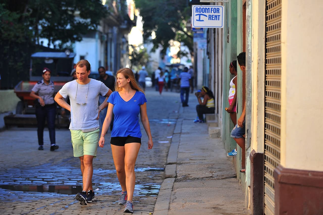 Tourists walk next to a house with a private room for rent in Havana, on February 10, 2017. Tourists are facing inconveniences where they least imagined, in four and five star hotels in Cuba. The boom in tourism is putting Cuba under pressure. / AFP / YAMIL LAGE / TO GO WITH AFP STORY BY RIGOBERTO DIAZ (Photo credit should read YAMIL LAGE/AFP/Getty Images)