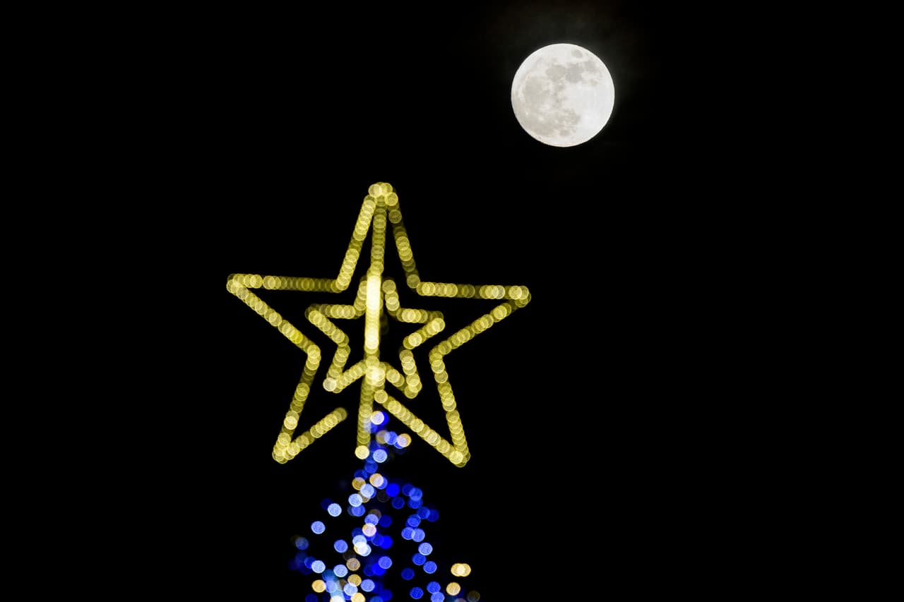 <b>Bulgaria.</b> La superluna se luce junto a la estrella que corona un árbol de Navidad en Sofía, capital búlgara.