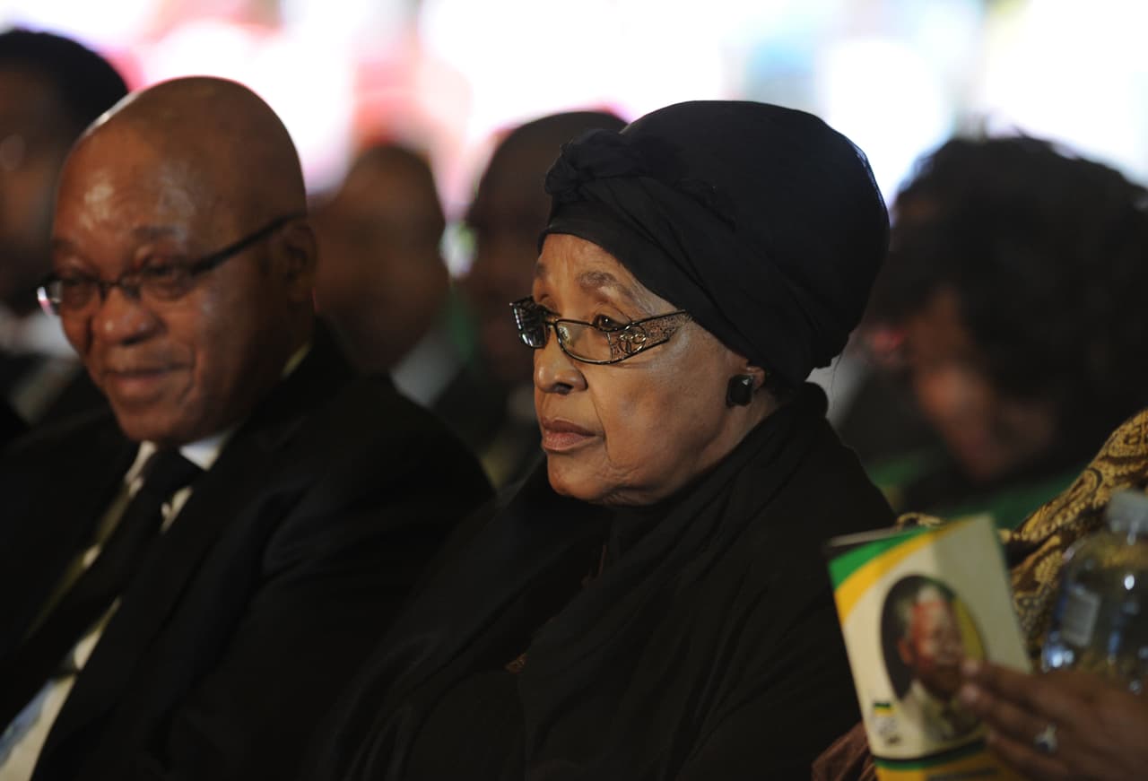 En su informe final, la Comisión de la Verdad y Reconciliación dictaminó que Madikizela-Mandela era "política y moralmente responsable de las graves violaciones de los derechos humanos cometidas por el MUFC", una milicia creada por la activista a la que se le atribuye responsabilidad en varias muertes y torturas durante los años finales del apartheid. En la fotografía Madikizela-Mandela acompaña al expresidente surafricano Jacob Zuma en los funerales de Estado de Nelson Mandela, quien falleció en 2013.