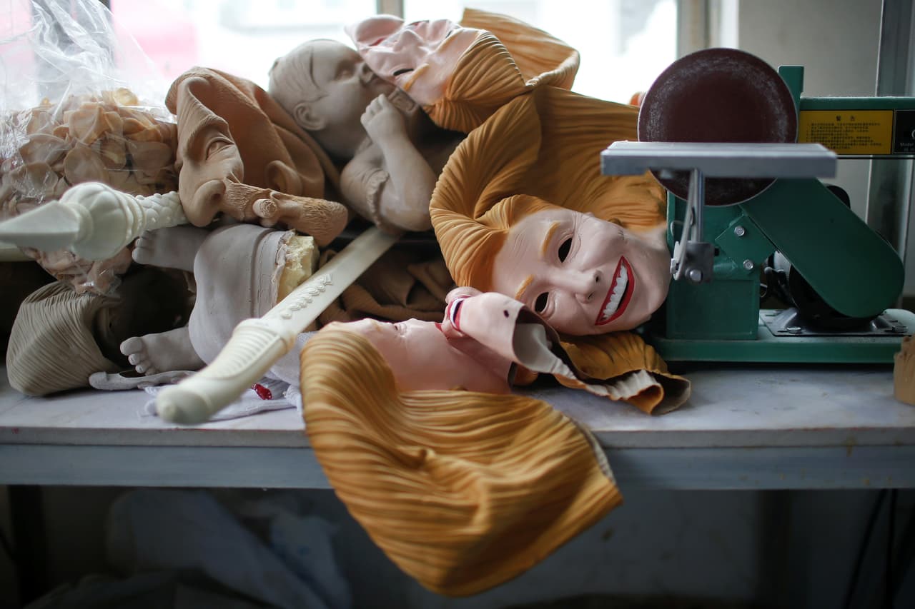 Dentro de la fábrica se encuentran rostros de Hillary Clinton apilados junto a otros moldes y máscaras sin color.