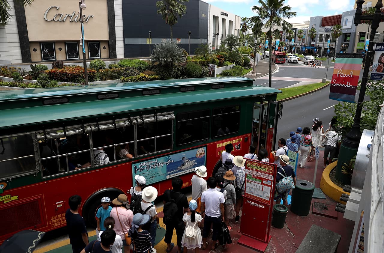 Turistas suben a un servicio de buses en el camino en Tamuning. En julio de 2017 llegaron a Guam más de 130,000 civiles, en su enorme mayoría por aire, detalla la 
<b><a href="https://www.guamvisitorsbureau.com/docs/research-and-reports/research/visitors-report/fy-2017/july-2017-preliminary-arrival-summary.pdf">Oficina de Visitantes</a></b>.