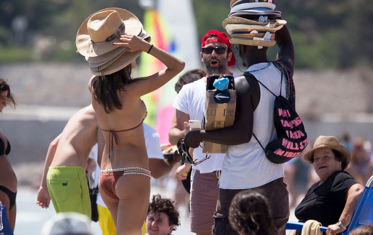Alessandra Ambrosio lleva más de una semana en las playas de Ibiza disfrutando del verano español. Aquí, la modelo de 36 años bromea con un vendedor de sombreros en la playa.