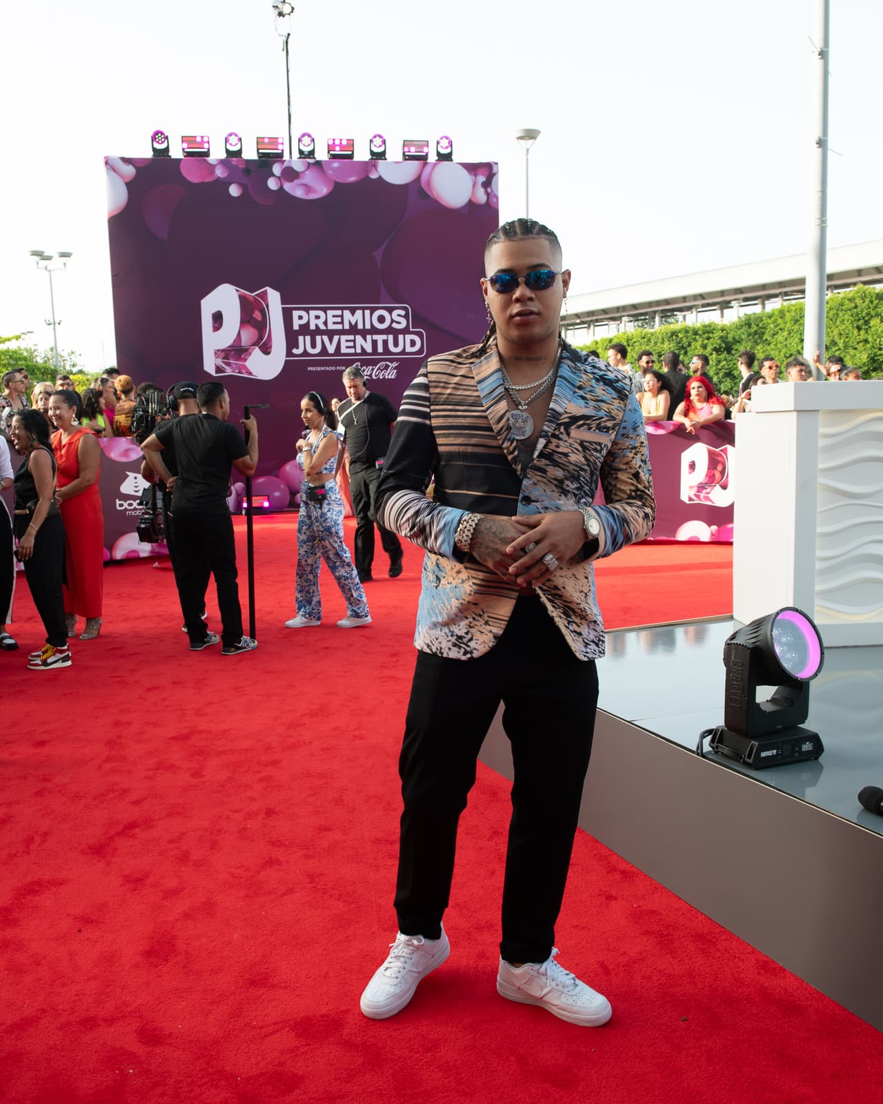 El cantante 
<b>Boza </b>escogió una chaqueta con estampado a rayas, pantalones negros, tenis blancos, gafas oscuras y cabello trenzado.