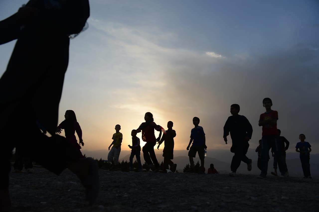 Un grupo de niños corre al atardecer para ver la bandera afgana más grande de Afganistán, levantada en Kabul por el presidente afgano Hamid Karzai en 2014.