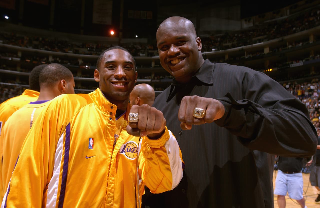 Kobe Bryant y Shaquille O'Neal muestran sus anillos de campeón de la NBA antes de la apertura de la temporada contra los Spurs de San Antonio en el Staples Center el 29 de octubre de 2002 en Los Ángeles, California.