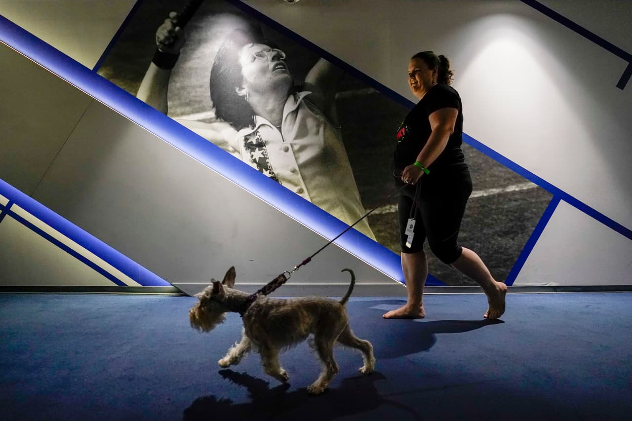 Una mujer camina con su mascota, al fondo una fotografía de la tenista Billie Jean King.