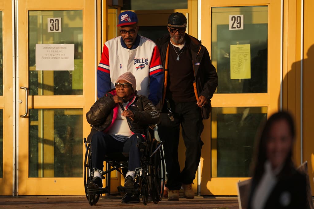 Liza Fortt, de 74 años, en el centro, acompañada por su hijo Timothy Walker, en el centro arriba, y su esposo Willie Fortt, salen de su lugar de votación mientras sale el sol después de emitir su voto.