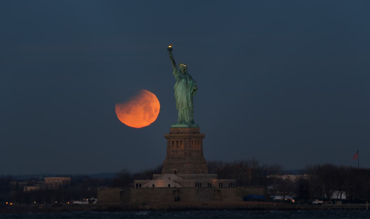 La luna enrojecida se contempla al lado de la Estatua de la Libertad. New York, New York, EEUU.