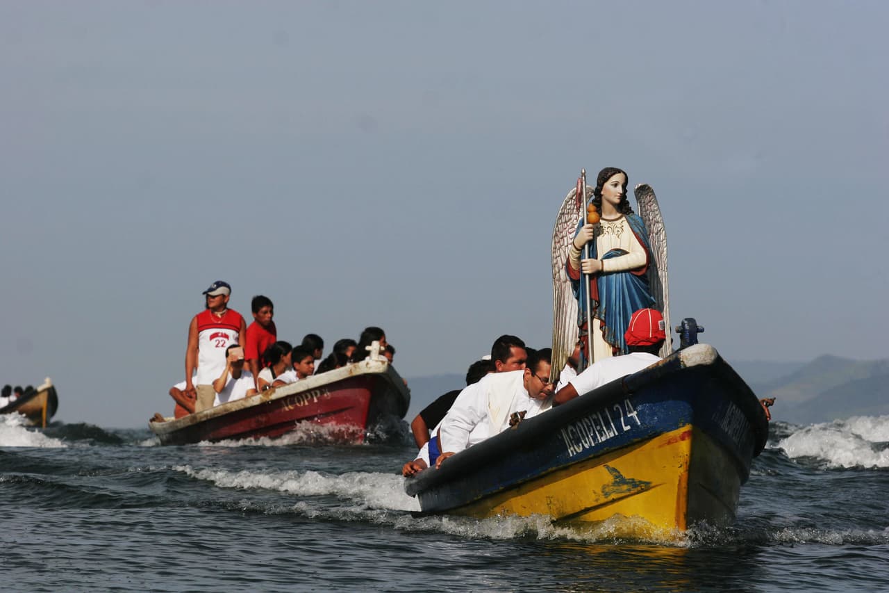 Aquí vemos unas embarcaciones en El Salvador que cargan con una antigua efigie del arcángel Rafael que sobrevivió una explosión en el puerto en 1934. La llevan hasta el frente de sus botes como amuleto de buena suerte durante su camino y procesión.