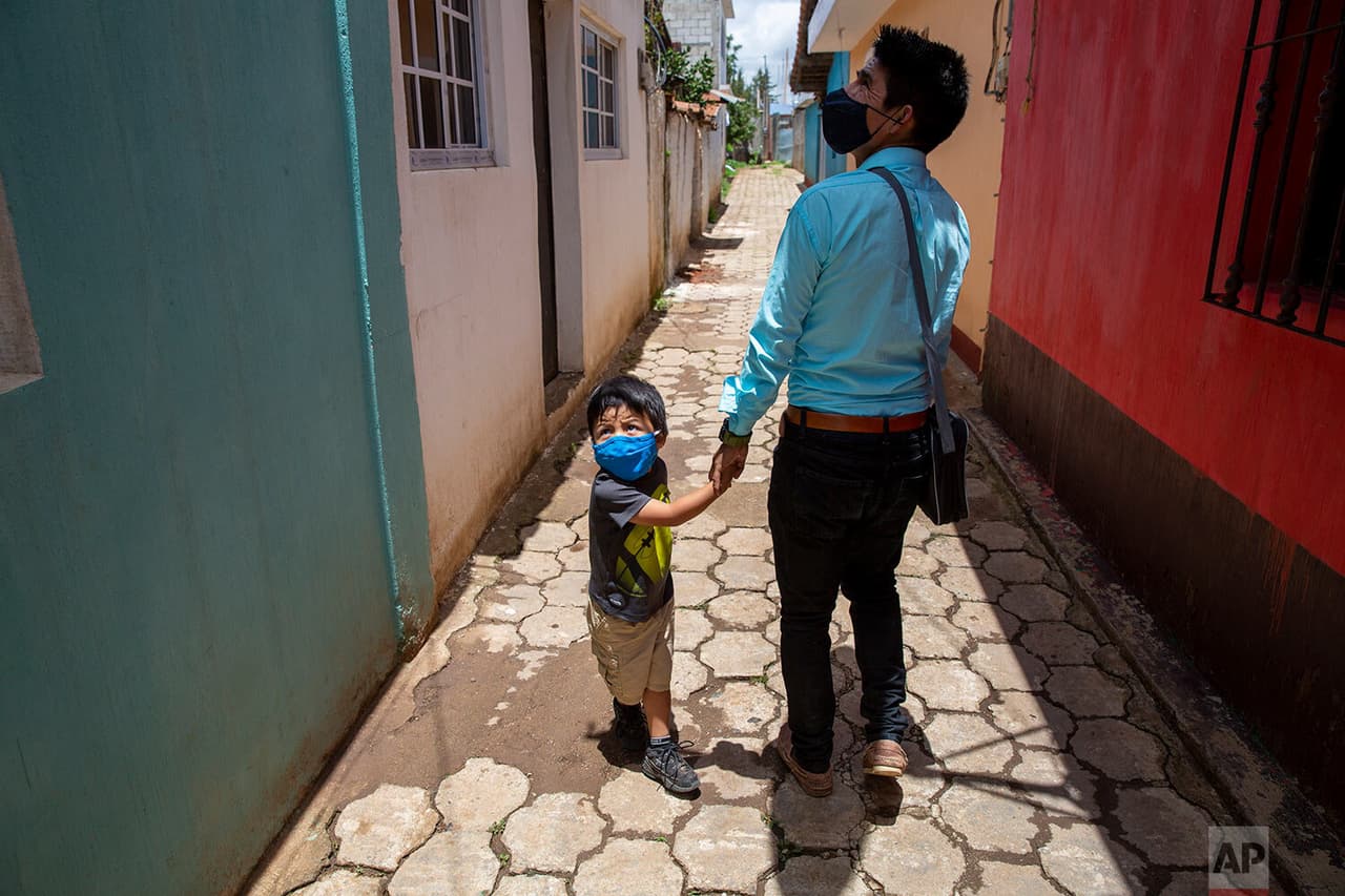 Gerardo Ixcoy y su hijo Dylan de tres años saludan a un vecino cuando el profesor llega a casa después de un día de dar clases individuales a sus estudiantes de sexto grado, 
<b>asegurándose de no violar el toque de queda establecido para evitar mayor propagación del <a href="https://www.univision.com/temas/coronavirus">coronavirus</a>. </b>
<br>