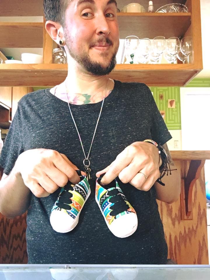 Trystan enseña unos zapatos para el bebé en camino.