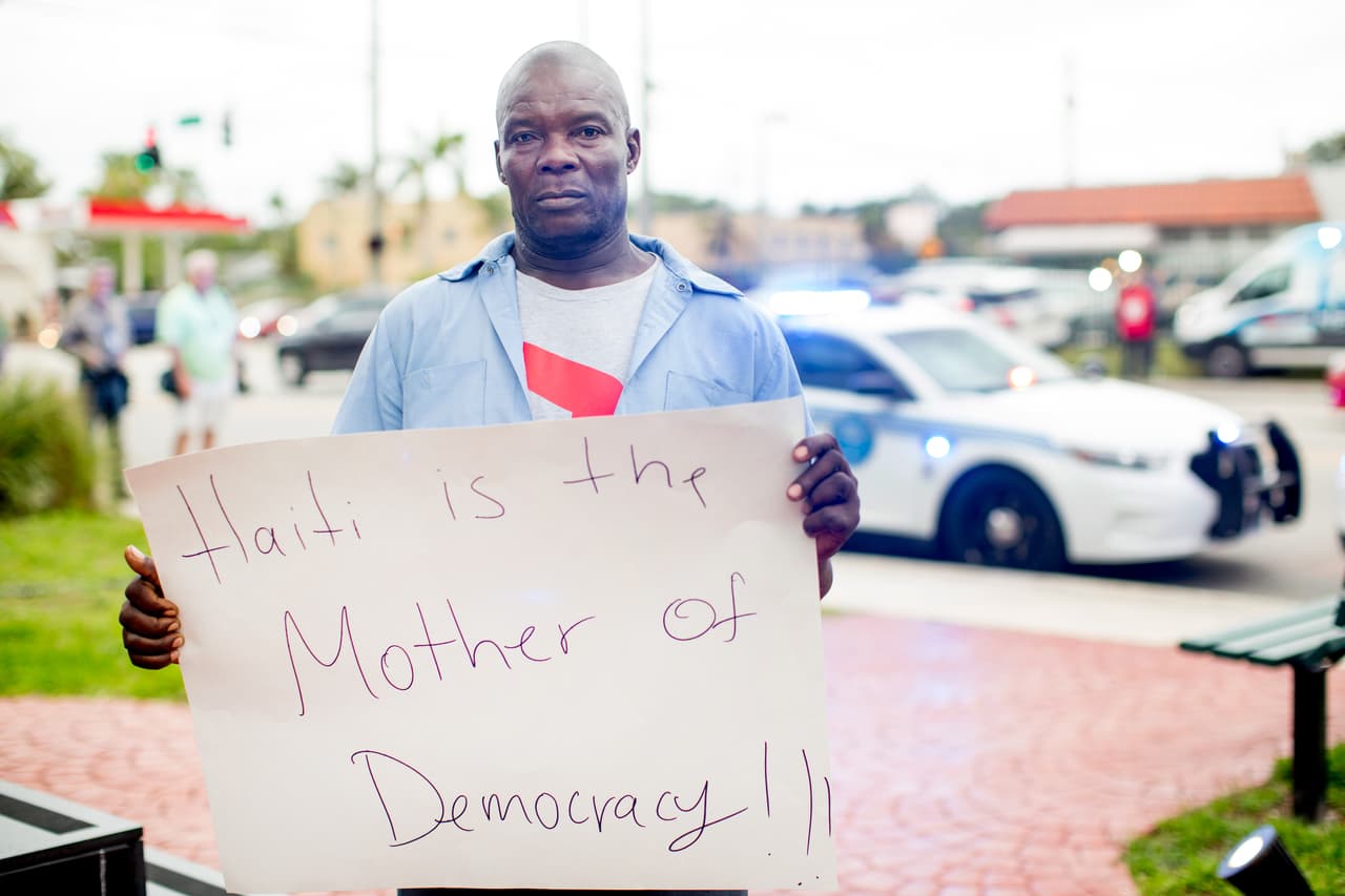 <b>Lucien Roussel</b> tiene 25 años en EEUU y lleva un cartel que tiene escrito en inglés 'Haití es la madre de la democracia'. “Hoy es un día triste por dos razones. La primera es la conmemoración de la tragedia, cada uno de los que estamos aquí perdió al menos un familiar en el terremoto. La segunda razón fueron las palabras del presidente. No importa lo que diga Donald Trump: somos buena gente, Haití es un gran país y los haitianos que estamos en EEUU somos trabajadores.