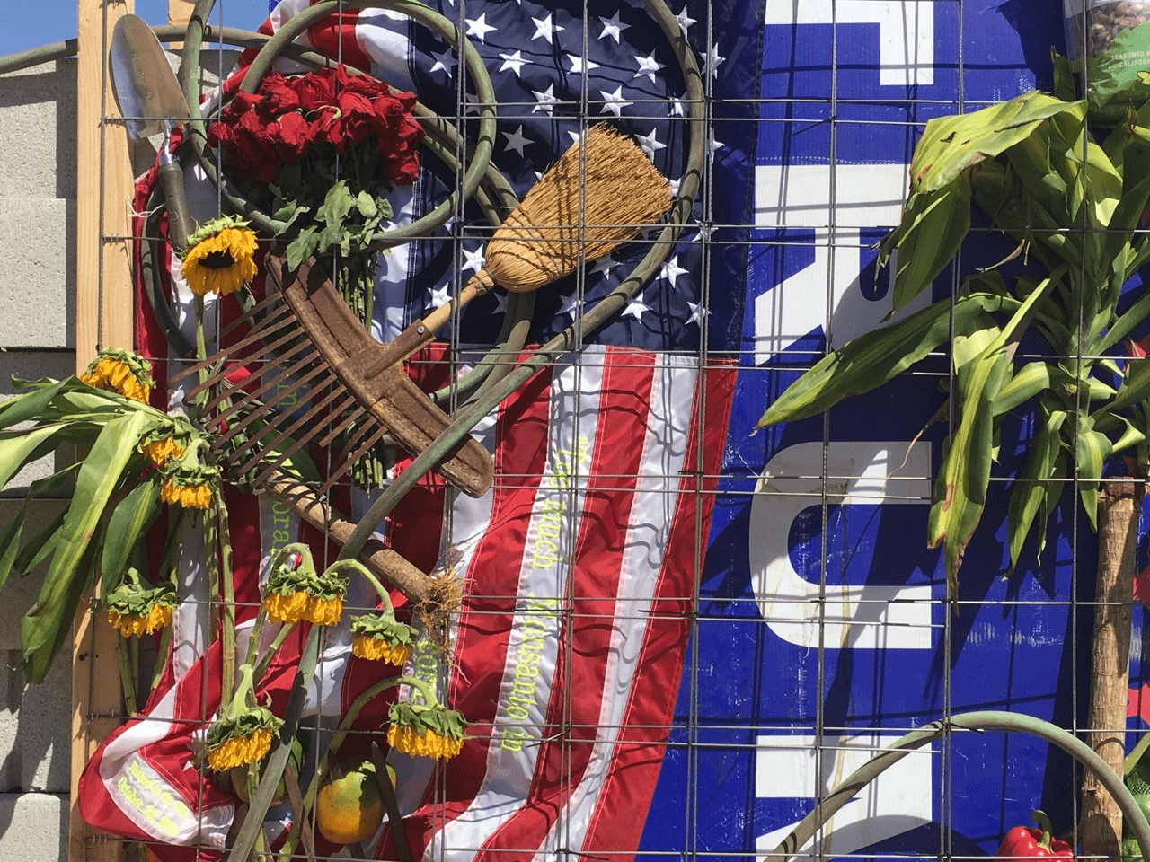 Elementos agrícolas, una bandera y un cartel de Trump en muro anti-Trump