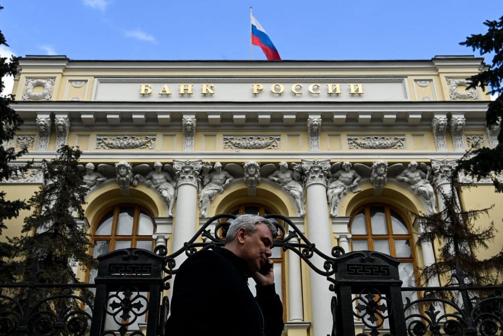Un hombre hablando por teléfono pasa por delante de la sede del Banco Central de Rusia mientras ondea la bandera rusa, en el centro de Moscú.