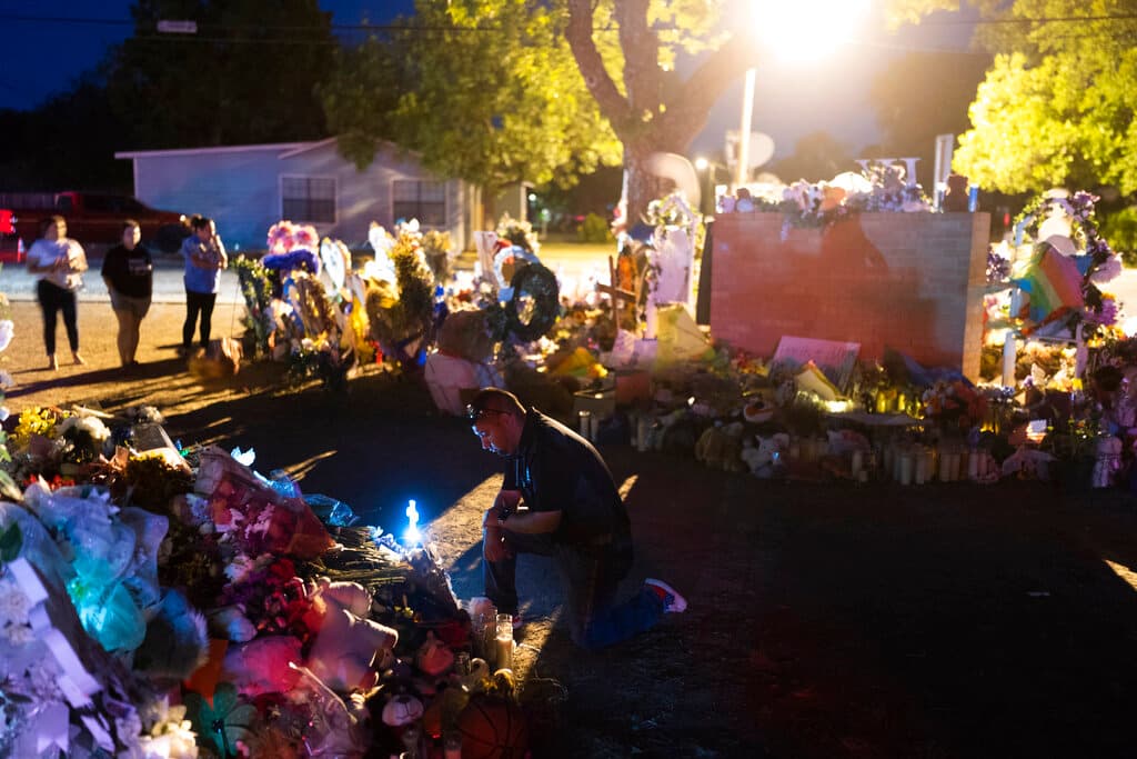 Un hombre se arrodilla frente a un montículo de flores en un monumento en la escuela.