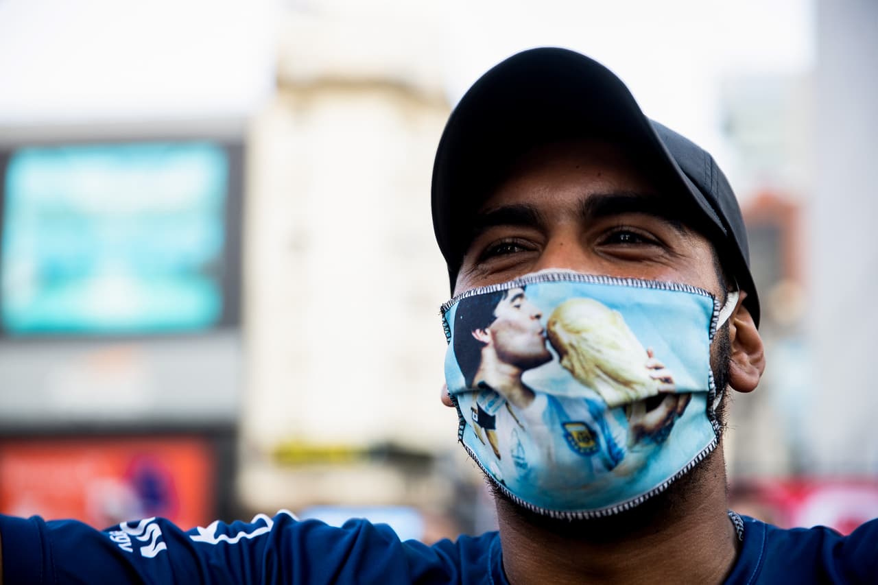 Un hombre utiliza una máscara con la imagen de Maradona besando la siempre codiciada Copa del Mundo de la FIFA, mientras entona cantos alusivos al excapitán de la Selección Argentina de Fútbol.