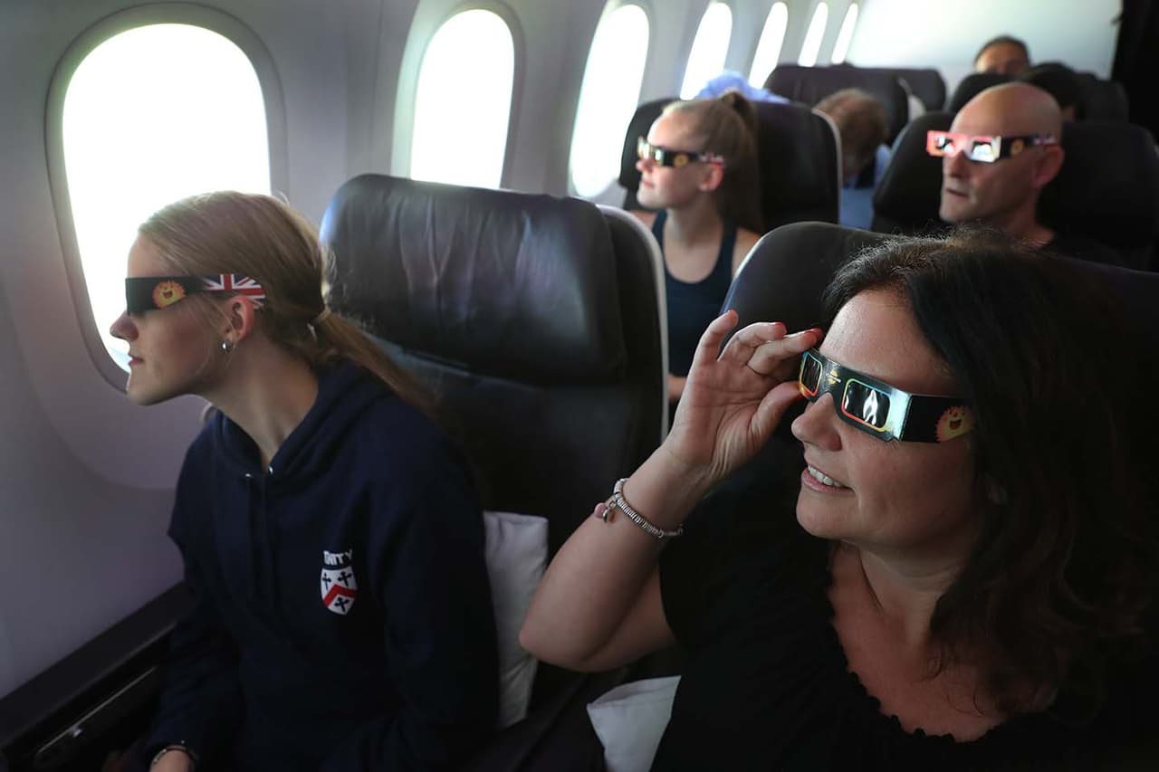 Nicola James, de 49 años, con sus dos hijas de 18 años, Holly (adelante a la izquierda) y Grace (detrás) observan el inicio del eclipse solar mientras vuelan sobre Estados Unidos a bordo del Boeing 787 de Virgin desde el aeropuerto Heathrow de Londres con destino a Miami.
