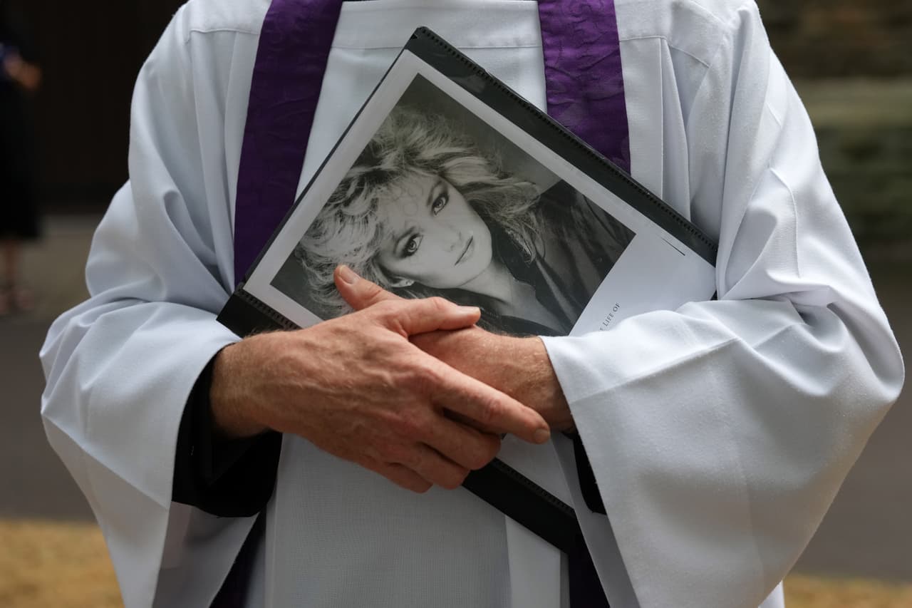 Un sacerdote no identificado sostiene un cartel de Bonnie Tyler frente a la iglesia de Santa María en Swansea, Gales, el lunes 17 de agosto de 2026, antes del servicio religioso y el funeral de la música, cuyo nombre real era Gaynor Hopkins.