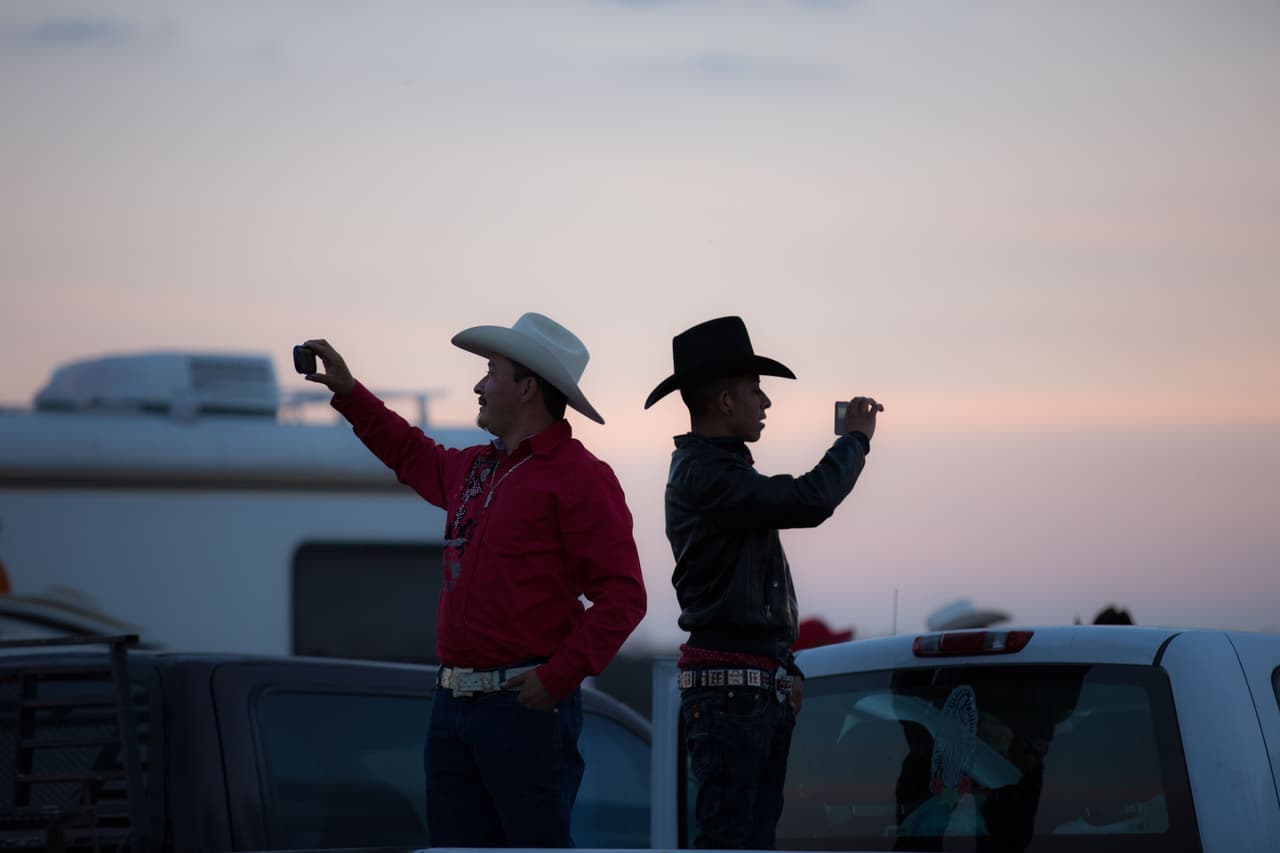 Dos asistentes de la fiesta graban video con su celular de la explanada en Laguna Seca donde se realizó la carrera de caballos, en la que murió un hombre, y los conciertos.
