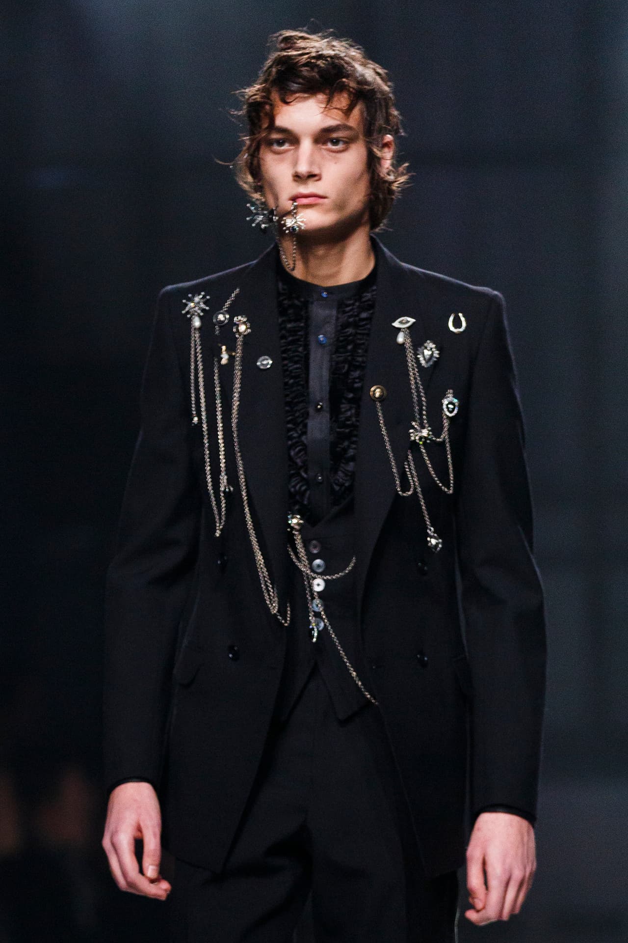 Pocas firmas más lúdicas que la de Alexander McQueen, cuya genialidad sobrevive en su colección Otoño-Invierno 2016-2017, con trajes como este, adornado con largas cadenas plateadas que cuelgan de broches, como si el saco mismo tuviera 
<i>piercings</i> (amigos cercanos de los tatuajes, 
<i>guiño-guiño</i>).
<br>