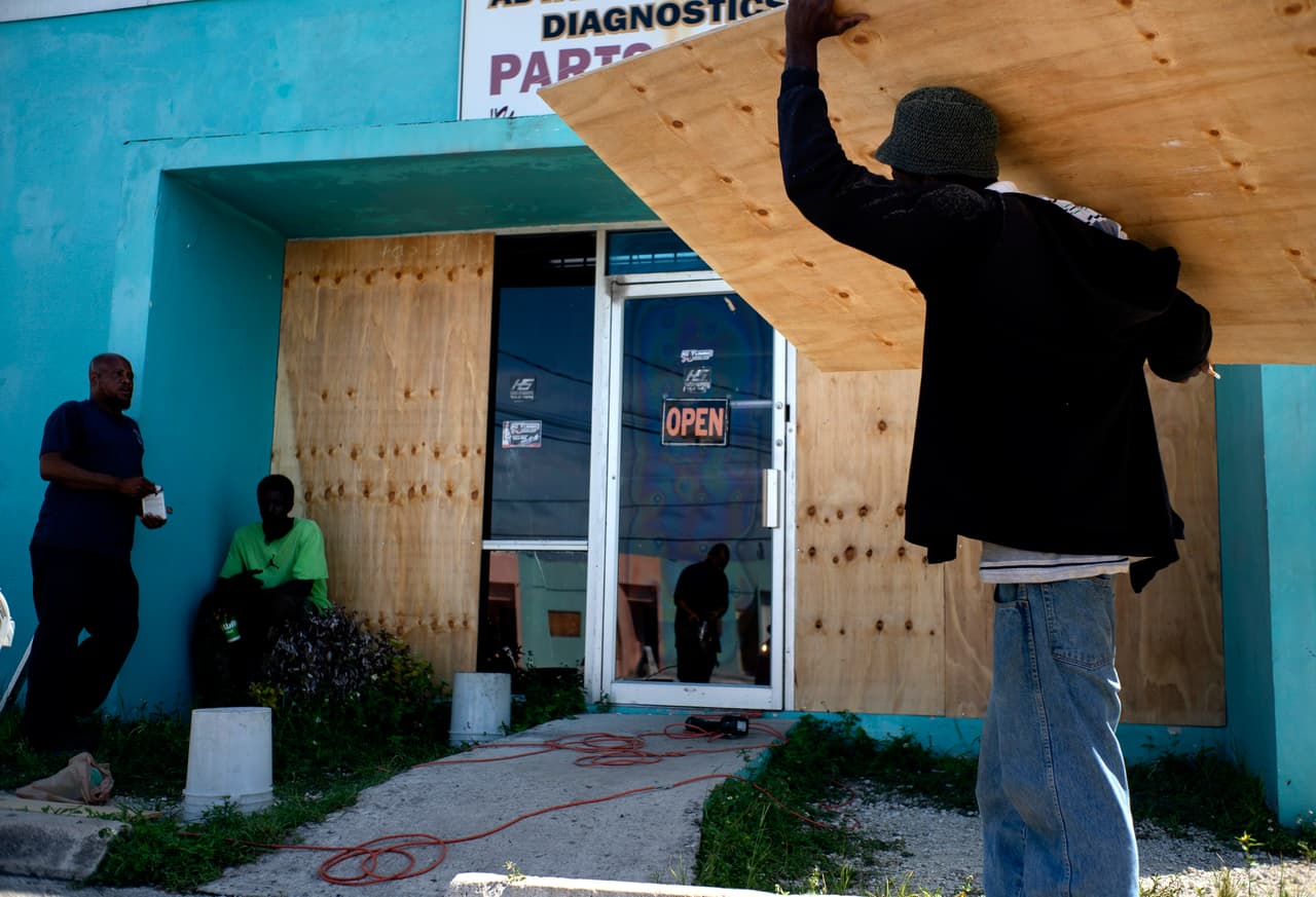 Trabajadores tapan con madera las ventanas de un negocio en Freeport, en preparación para la llegada de Dorian.
