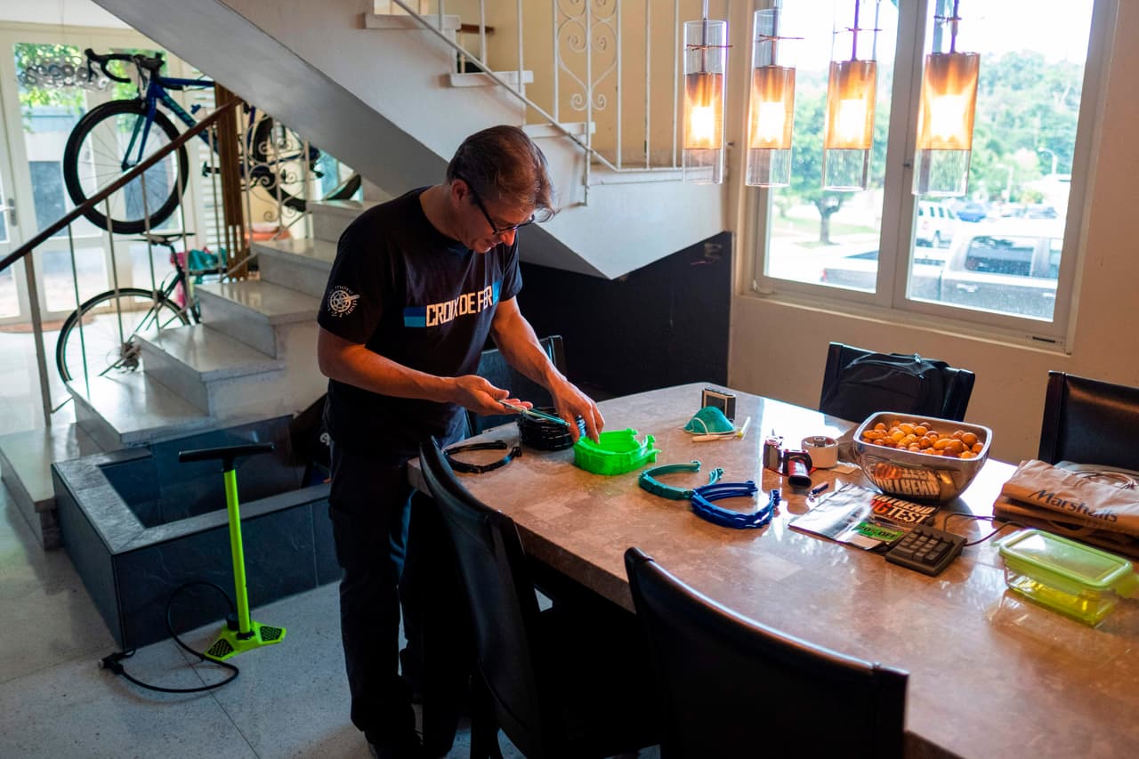 El Dr. Jonathan Alistair clasifica marcos impresos en 3D recientemente acabados para protectores faciales en su comedor.