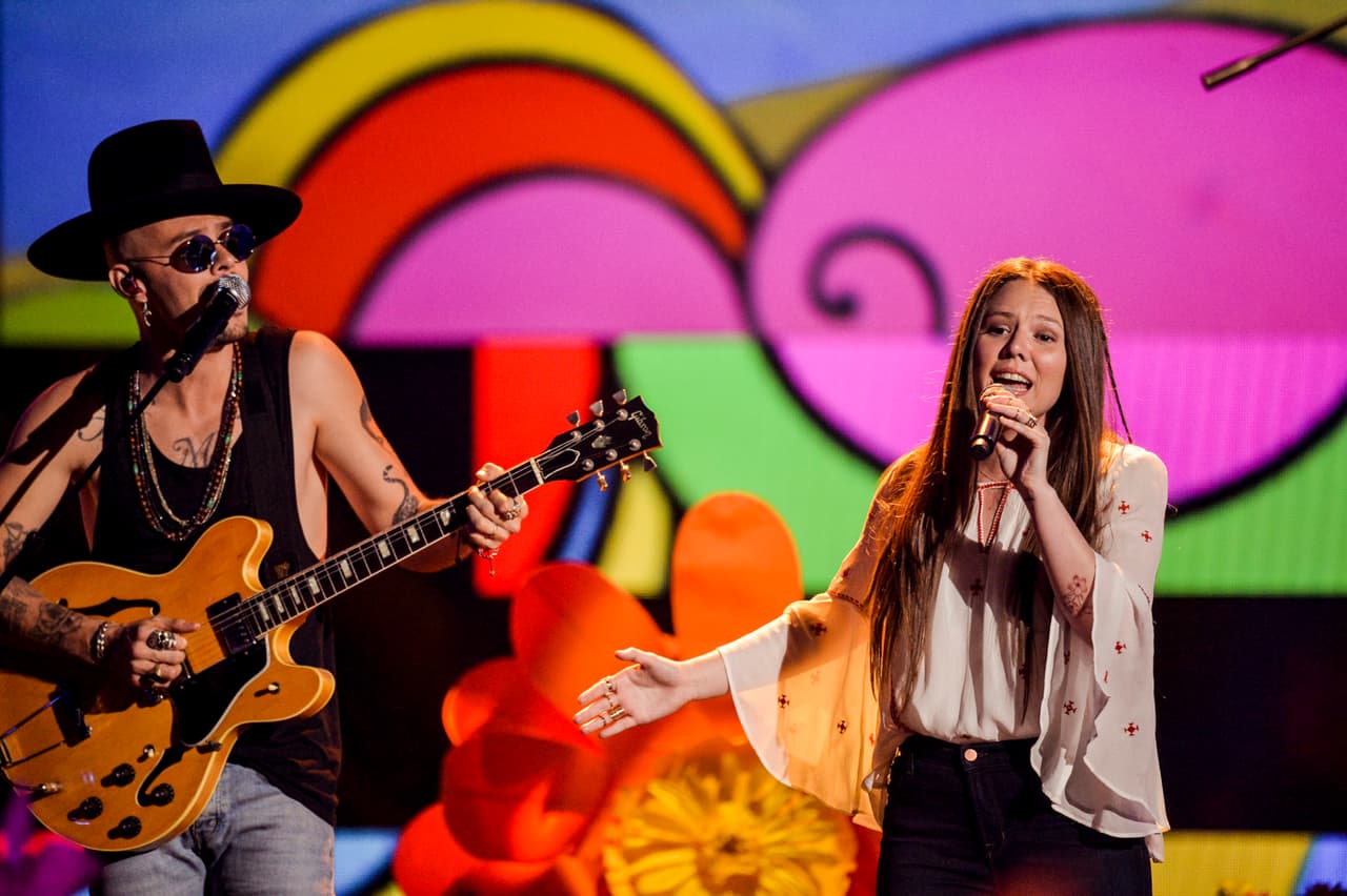 Para su presentación Joy se soltó el pelo y lo peinó con raya en medio. Las trenzas le dieron un toque más bohemio a su melena. El maquillaje fue súper natural, destacaron ligeramente las sombras rojizas, pero no logramos percibir delineado alguno ni capas exageradas de máscara de pestañas. Los labios los llevó en nude.