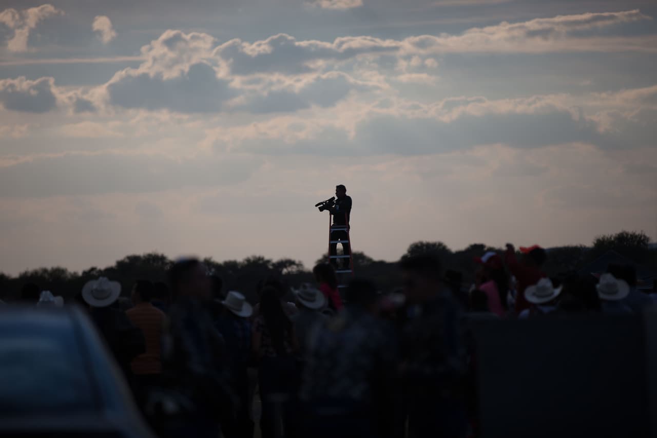 Un videógrafo se prepara para filmar la carrera de caballos de los XV de Rubí subido a una escalera.