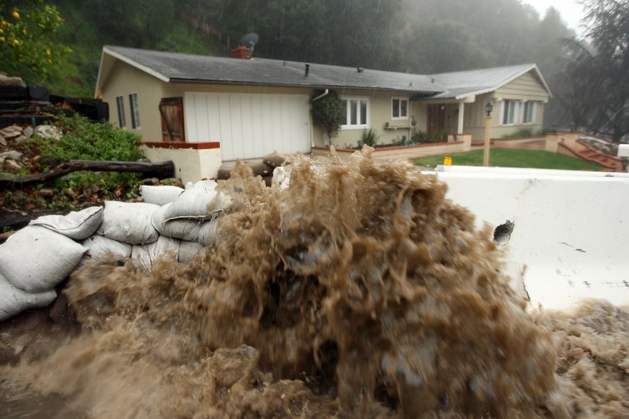 LA CANADA FLINTRIDGE, CA - JANUARY 21: Muddy water hits sand bags and a K rail in front of a house threatened with mud slides from the hill behind it during the fourth storm of the week on January 21, 2010 in La Canada Flintridge, California. Hundreds of homes have been evacuated because of the threat of major mud slides and debris flows below foothills and mountains that burned last year. Despite warnings by firefighters that they will not be able to get through debris flows to rescue stay-behind residents if a major event occurs, many refuse to leave. The threat is particularly high near the San Gabriel Mountains which were denuded of natural flood-controlling vegetation by the 250-plus square mile Station Fire. (Photo by David McNew/Getty Images)