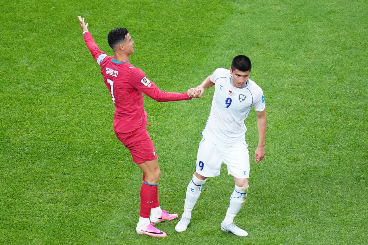 Odiljon Xamrobekov (9) de Uzbekistán ayuda a Cristiano Ronaldo (7) de Portugal a levantarse durante el partido de fútbol del Grupo K de la Copa Mundial