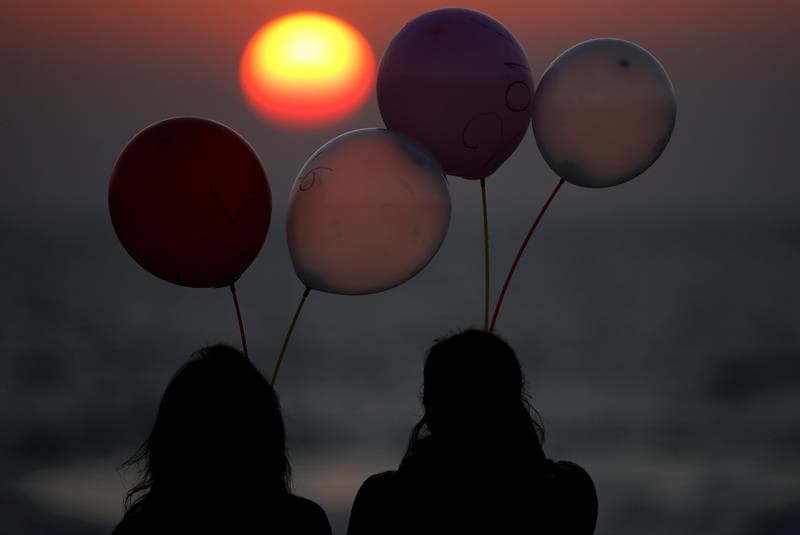 Dos jóvenes palestinas observan el atardecer mientras sostienen globos marcados con el año 2016.
