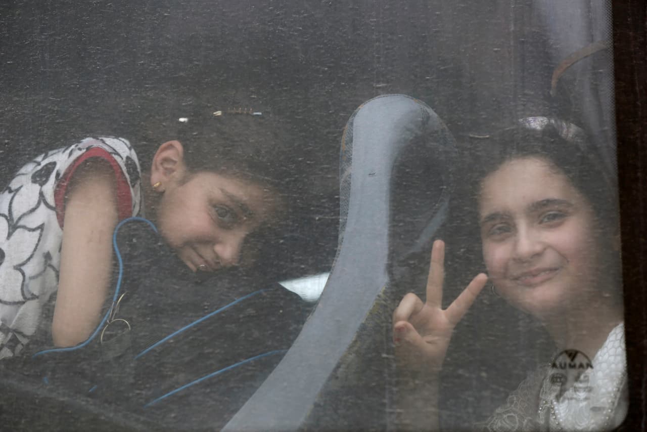 Dos niñas sonríen a la cámara a pesar de estar saliendo de su casa en ruta al campo de refugiados.