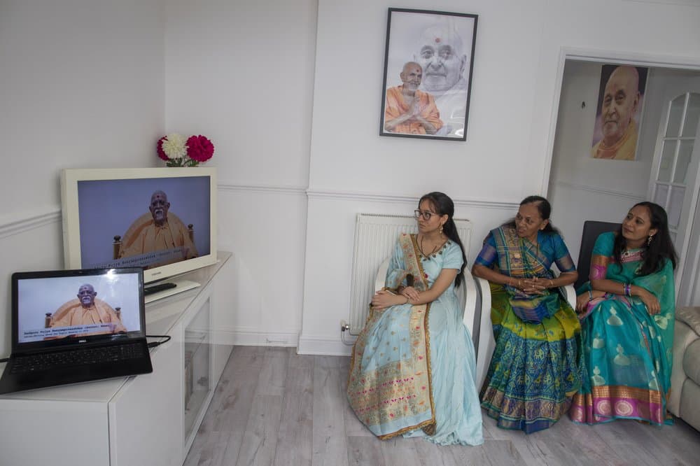 Aagna Patel, Pushpa Patel, y Hemali Patel vestidas con sus saris, escuchan
<b> a Guru Pujya Swayamprakashdas hablar con ellas a través de la pantalla de televisión en la comodidad de su sala de estar en su casa suburbana en Hemel Hempstead, Inglaterra.</b> "Eso es lo que nos hubiéramos puesto en el templo", dijo Hemali, "así que nos pareció correcto vestirse para la ocasión".