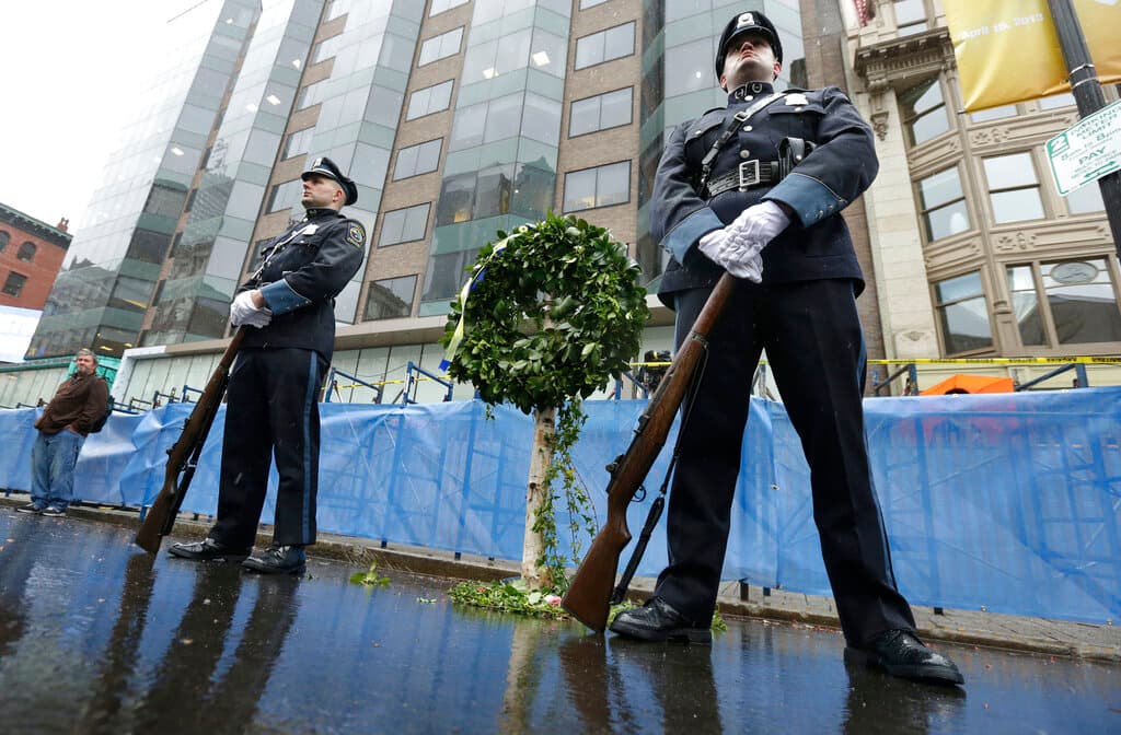 Agentes de policía de Ashland, Massachusetts, custodian una corona conmemorativa en el lugar de la primera explosión de bomba, cerca de la línea de meta del Maratón de Boston, el martes 15 de abril de 2014, en Boston.