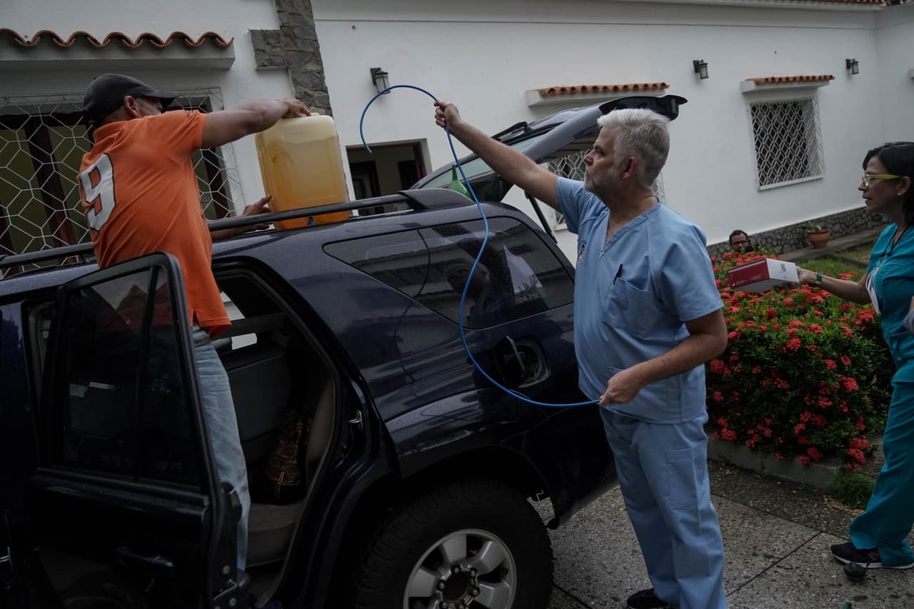 Dos médicos venezolanos llenan el tanque de su auto con un bidón de gasolina que consiguieron en medio de la escasez de combustible en el país petrolero. Ese día, viajarían a un operativo para atender a niños con desnutrición.