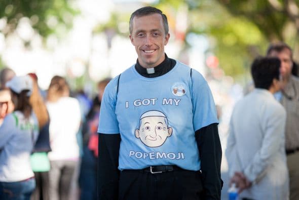 El padre Mateo Schneider posa sonriente con una caricatura del Papa en su camiseta.