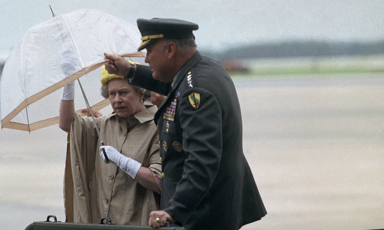 La reina Isabel II recibe un poco de ayuda con su paraguas del general H. Norman Schwarzkopf durante una lluvia en la Base de la Fuerza Aérea MacDill de Tampa en la mañana del lunes 20 de mayo de 1991. La reina hizo una breve visita para convertir a Schwarzkopf en caballero honorario antes viajar a texas. (Foto AP/Lynne Sladky)